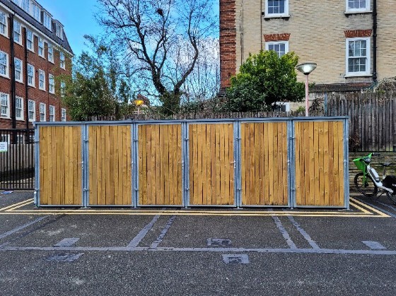 Bike sheds, with six tall wooden doors, installed in a car park on Margery Estate