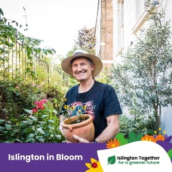 A man with a hat standing in his front garden, holding a pot with yellow flowers. He is looking at the camera and smiling. At the bottom there is a colourful bar saying 'Islington in Bloom' and 'Islington Together for a greener future'.