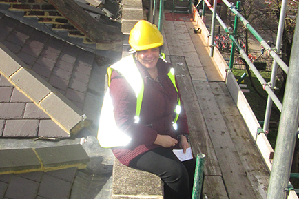 Ellie Achilleos, Capital Works Manager wearing a high vis jacket and a hard hat whilst sat on a roof at a construction site