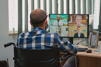 man wearing a blue check shirt, sitting away from the camera in a wheelchair and speaking to four collogues on a video conference call