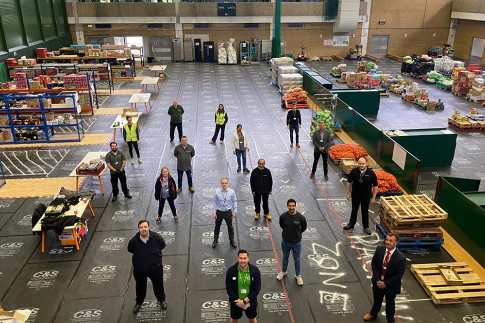 a group of Islington Council staff, standing socially distance in a food distribution warehouse, surrounded by packing stations and fresh produce