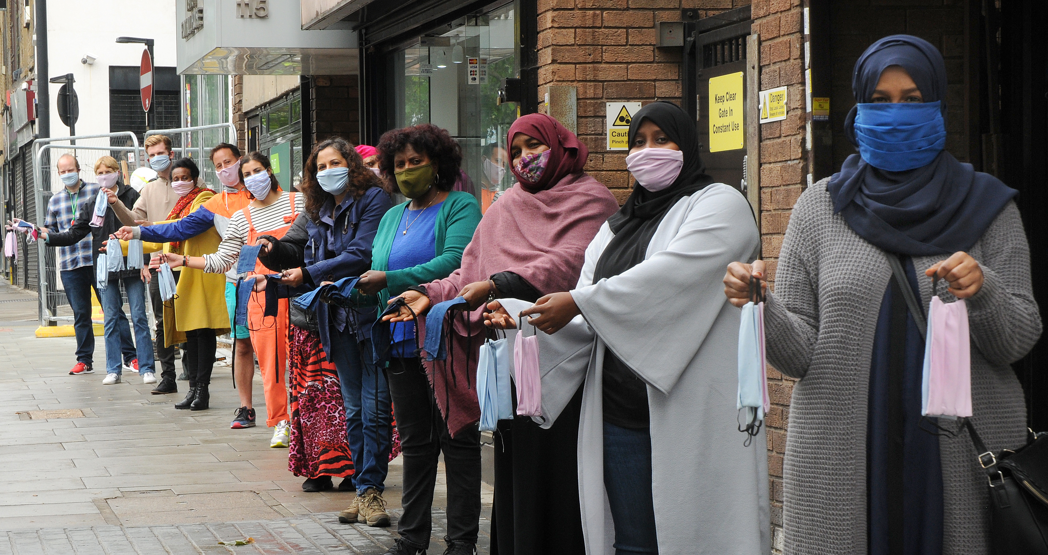 A community group of women wearing masks and holding up masks they have made