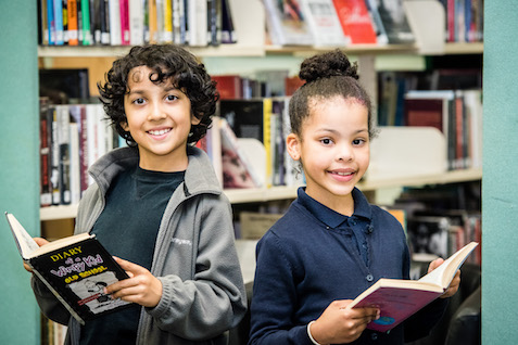 Two children in library holding books and facing the camera