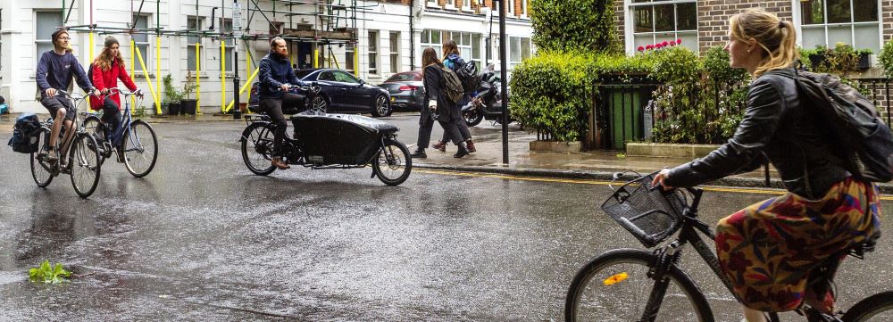 People cycling and walking on a wet residential street in Islington.