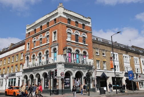 Buildings, including the Hope and Anchor theatre pub, and people crossing the road on Upper Street in Islington, London